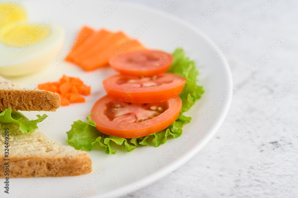 Boiled eggs, bread, carrots, and tomatoes on a white plate with a knife and fork.