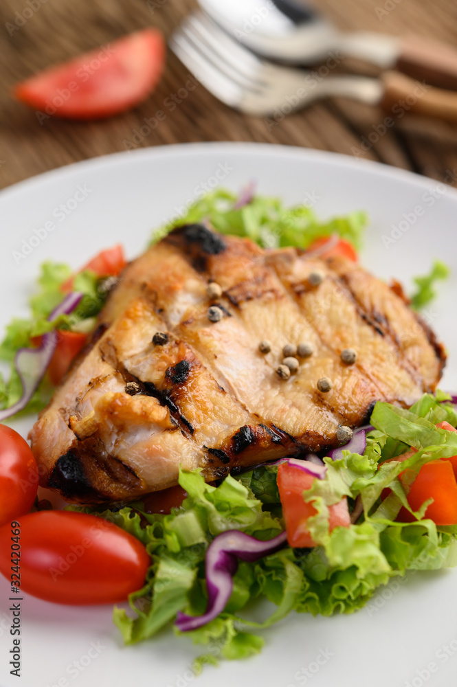 Grilled chicken on a white plate with a salad of tomatoes, carrots and chilies cut into pieces.