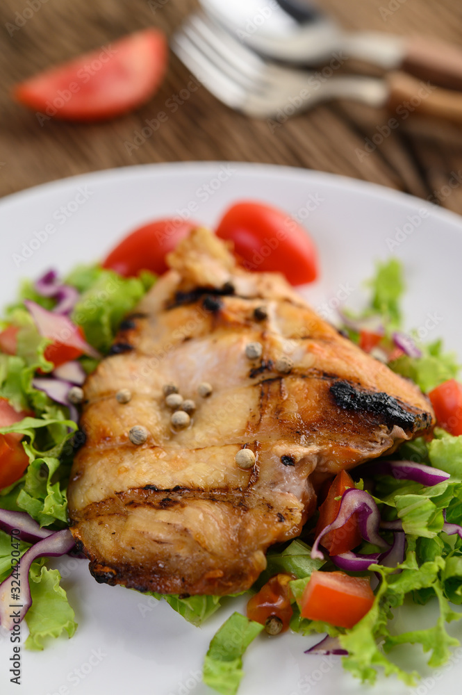 Grilled chicken on a white plate with a salad of tomatoes, carrots and chilies cut into pieces.