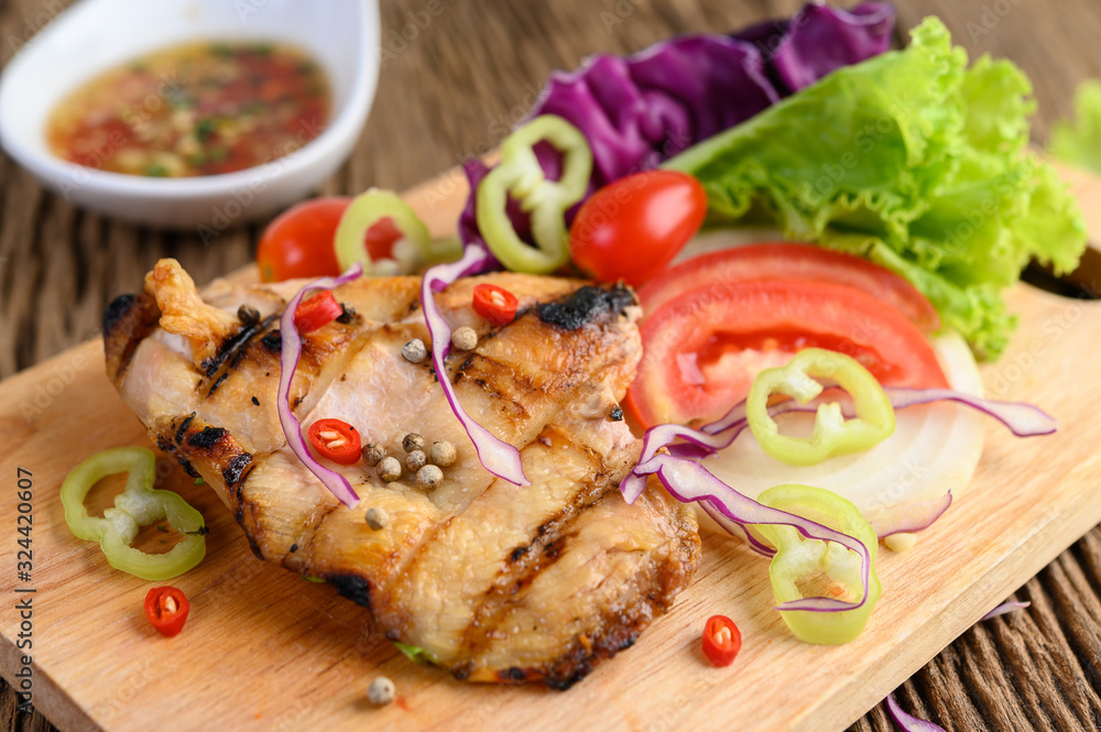 Grilled chicken on a Wood cutting board with salad, tomatoes, chilies cut into pieces, and sauce. Grilled chicken on a Wood cutting board with salad, tomatoes, chilies cut into pieces, and sauce.