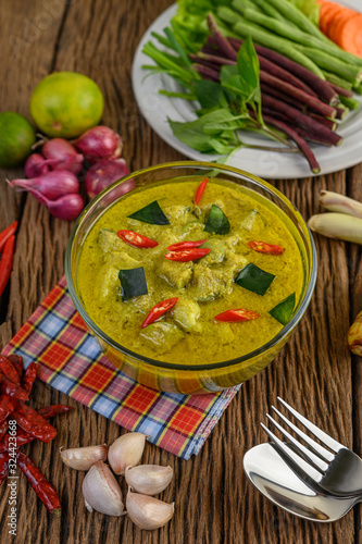 Green curry in a bowl with fork and spoon on wooden table.