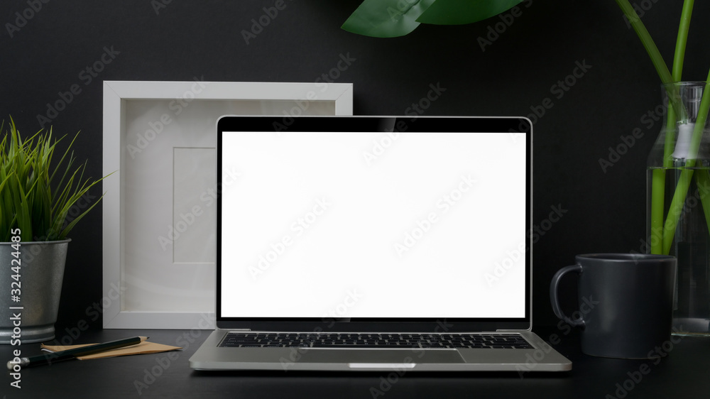 Close up view of trendy workplace with blank screen laptop on black table Close up view of trendy workplace with blank screen laptop on black table