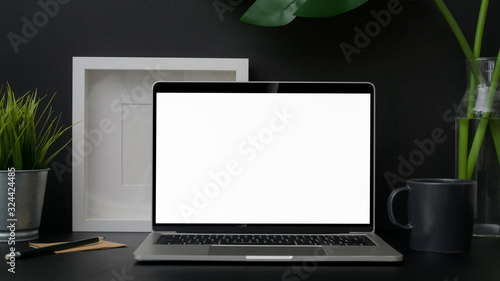 Close up view of trendy workplace with blank screen laptop on black table