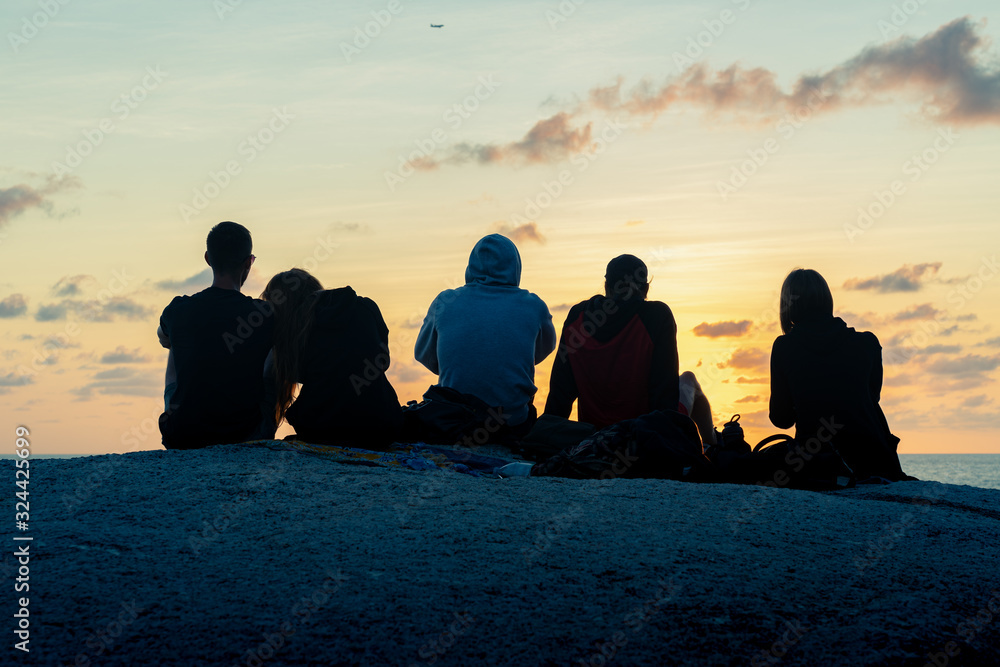 A group of young guys and girls meets dawn on a rock by the sea A group of young guys and girls meets dawn on a rock by the sea