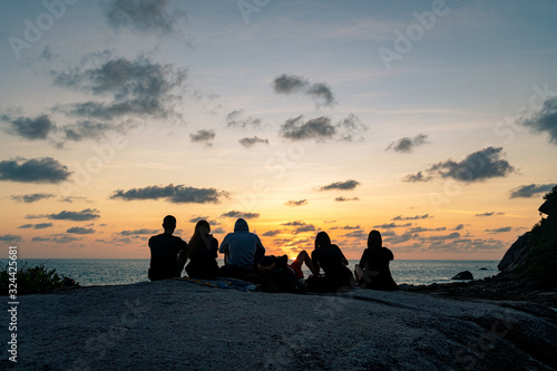 A group of young guys and girls meets dawn on a rock by the sea 