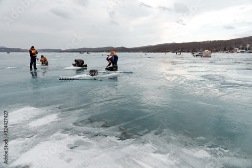A group of fishermen fish on ice on a thawing Big Lake. Krasnoyarsk region. Russia.