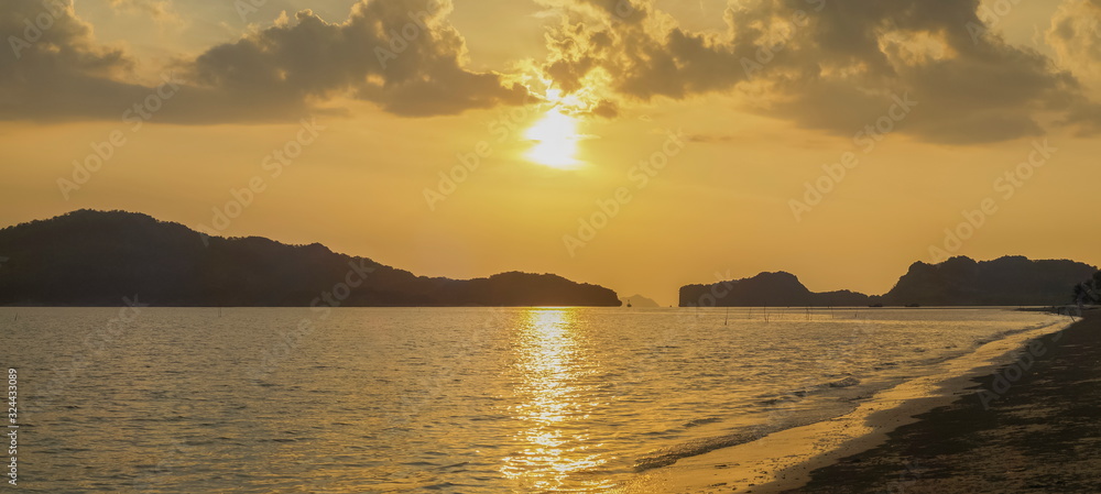 view panorama seaside evening on long beach of limestone mountain in the sea with yellow sun light and cloudy sky background, sunset at Pak Bara Beach, La-ngu District, Satun, southern Thailand.