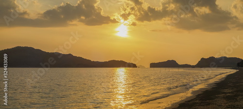 view panorama seaside evening on long beach of limestone mountain in the sea with yellow sun light and cloudy sky background, sunset at Pak Bara Beach, La-ngu District, Satun, southern Thailand.