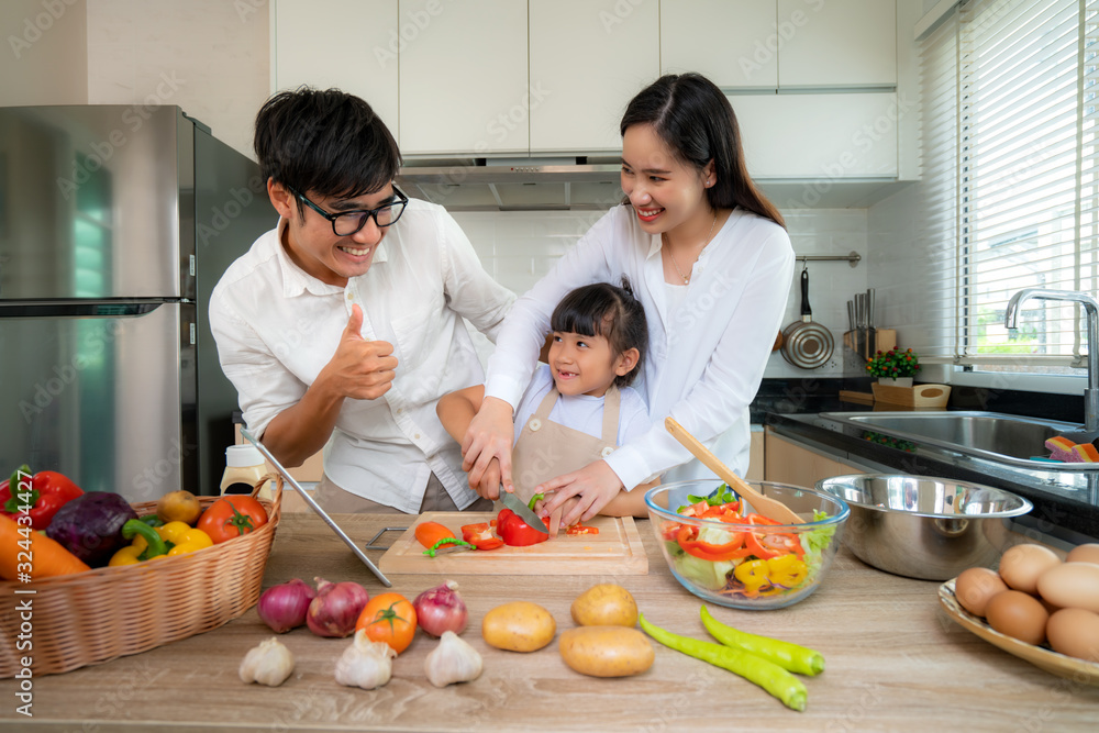 Asian mother teaching her daughter shredded vegetable salad with father thumb up on the side while the family was cooking in the kitchen at home. Family life love relationship. Asian mother teaching her daughter shredded vegetable salad with father thumb up on the side while the family was cooking in the kitchen at home. Family life love relationship.