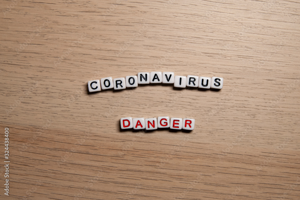 the word CORONAVIRUS DANGER in white cubes on a light wooden background. Corona Virus design template the word CORONAVIRUS DANGER in white cubes on a light wooden background. Corona Virus design template