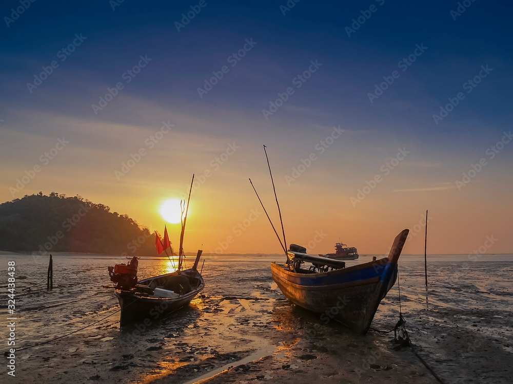 view seaside morning silhouette fishing boats on the beach with yellow sun light and blue sky background, sunrise at Mu Ko Phetra National Park, pak nam, la-ngu district, Satun, Thailand.