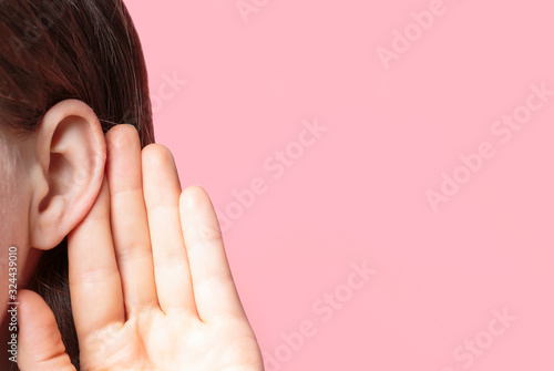 Quadro su tela The girl listens attentively with her palm to her ear close-up on pink backgroun