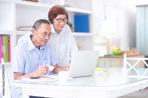 Asian senior couple using credit card for shopping online in front of computer.Technology and old people concept