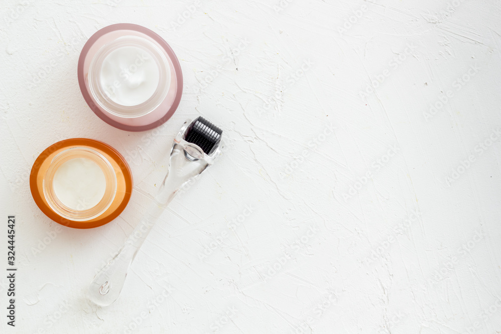 Dermaroller for mesotherapy near creams on white background top-down copy space