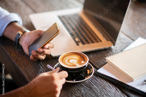 professional businessman using smart phone, Close-up of male hands working on line business in coffee shop with coffee cup and business stationary and communication gadgets on desk.successful - image
