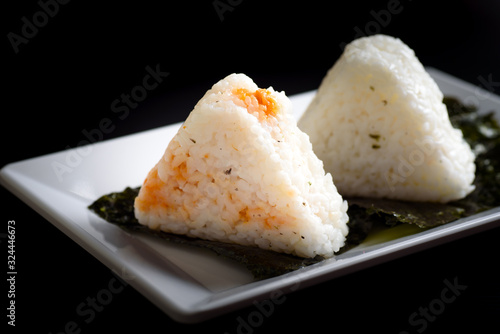 Onigiri, a Japanese food that looks like a triangle or ball oval Wrapped in seaweed (Nori), is a healthy food placed on a white plate with a black background