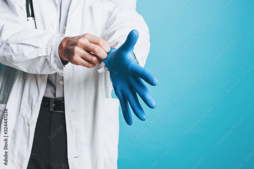 Crop photo of man doctor in white coat puts on rubber medical gloves isolated on blue background Crop photo of man doctor in white coat puts on rubber medical gloves isolated on blue background
