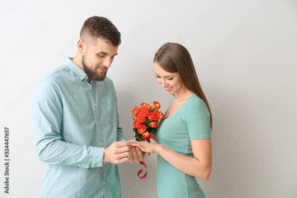 Young man putting ring on finger of his fiancee after marriage proposal on light background Young man putting ring on finger of his fiancee after marriage proposal on light background