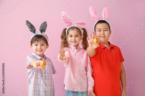 Little children with Easter eggs and bunny ears on color background