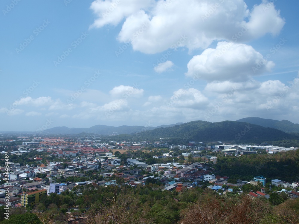 Panoramic view of Phuket city from above in sunny day. Phuket old town top view. Beautiful white clouds on a blue sky. Hills and water on a horizon. Thailand coastal city. Small town in Thai island 