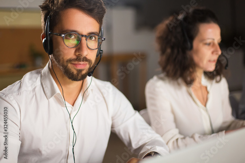 Handsome call center operator in eyeglasses looking at camera. Confident young man looking at camera. Call center concept