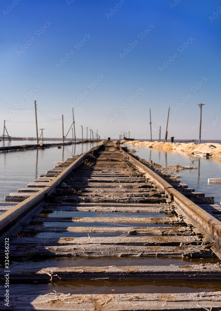 old rails go into the distance in the water against a blue sky. Nature destroys what man has built. Desolation, devastation. 