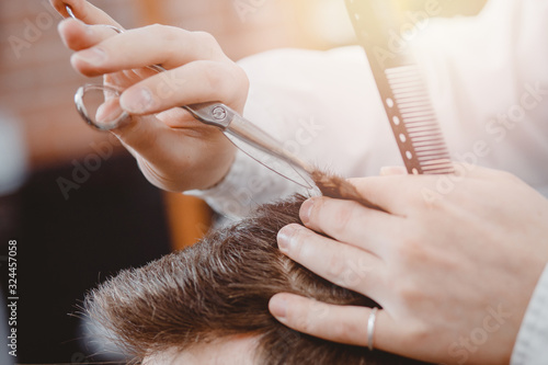 Close up of male hairdresser cutting hair with scissors, brown tinting, barber shop concept