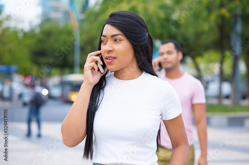 Front view of focused woman talking on smartphone. Attractive brunette talking to interlocutor through modern phone on street. Communication and technology concept