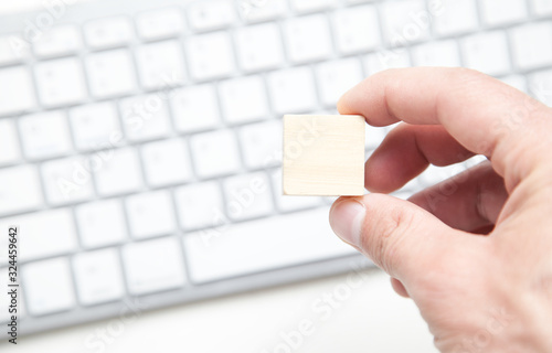 Male hand holding wooden blank cube on computer keyboard.