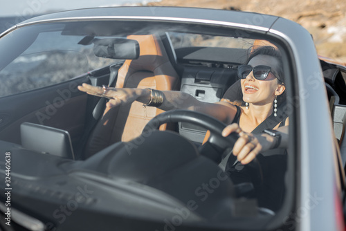 Portrait of a young woman driving a cabriolet near the ocean on a summer time. View through the windshield. Concept of a carefree travel and summer time