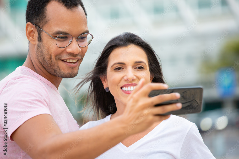 Happy multiracial friends taking self portrait with smartphone. Cheerful couple posing for selfie on street. Concept of self portrait Happy multiracial friends taking self portrait with smartphone. Cheerful couple posing for selfie on street. Concept of self portrait