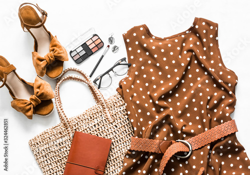 Polka dot summer brown dress, suede wedge sandals, eco straw tote bag, cosmetics on a light background, top view. Women's clothing set