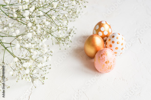 Close up of rose, white and golden decorated eeaster eggs with gypsophila on white concrete background. Copy space for text photo