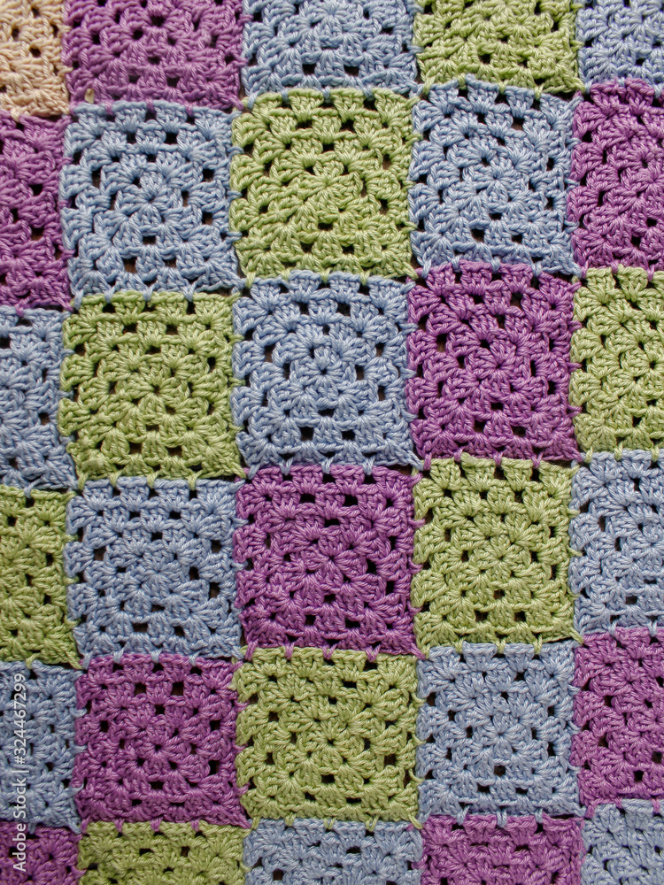 Crocheted element of green, purple, blue, beige flowers on an old wooden natural background. Screensaver for the desktop. Needlework, handmade, hobbies, free time.