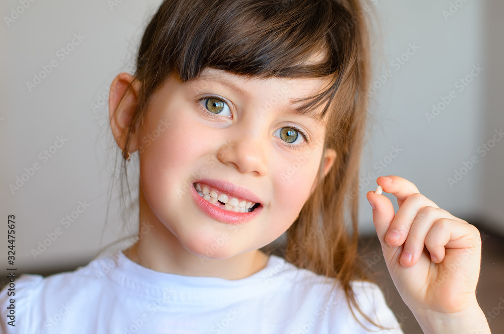 Cute preschooler showing her milk tooth fell out and her growing permanent tooth in open mouth. Beautiful smiling preschool girl holds in hand her first dropped baby tooth. Dental hygiene concept Cute preschooler showing her milk tooth fell out and her growing permanent tooth in open mouth. Beautiful smiling preschool girl holds in hand her first dropped baby tooth. Dental hygiene concept