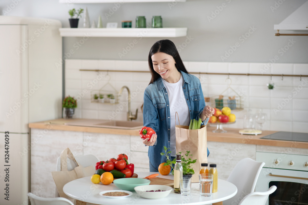 Young woman in front of kitchen table with vegetables and fruits.