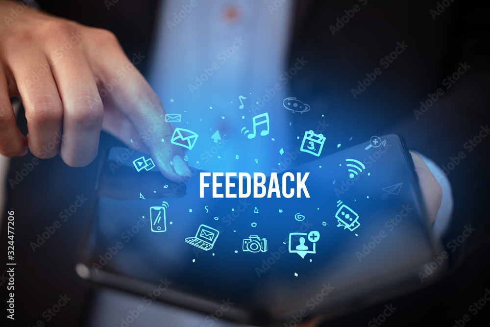 Businessman holding a foldable smartphone with FEEDBACK inscription, social media concept Businessman holding a foldable smartphone with FEEDBACK inscription, social media concept