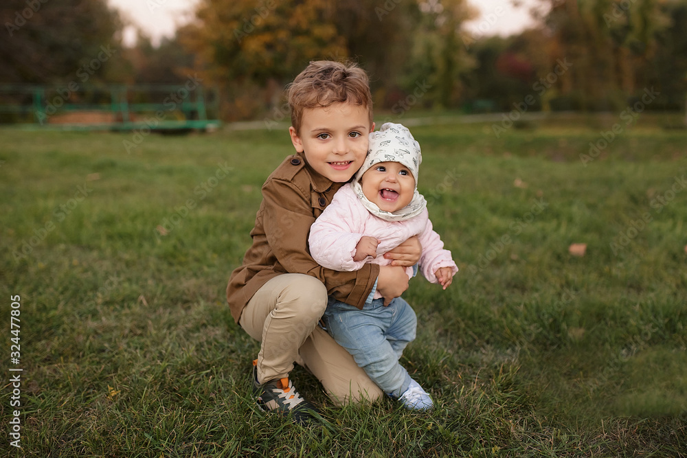 A little boy dressed in a brown coat smile and hug a his sister A little boy dressed in a brown coat smile and hug a his sister