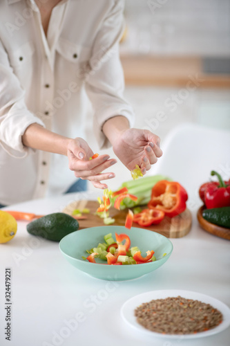 Female hands pouring shredded vegetables into a plate.