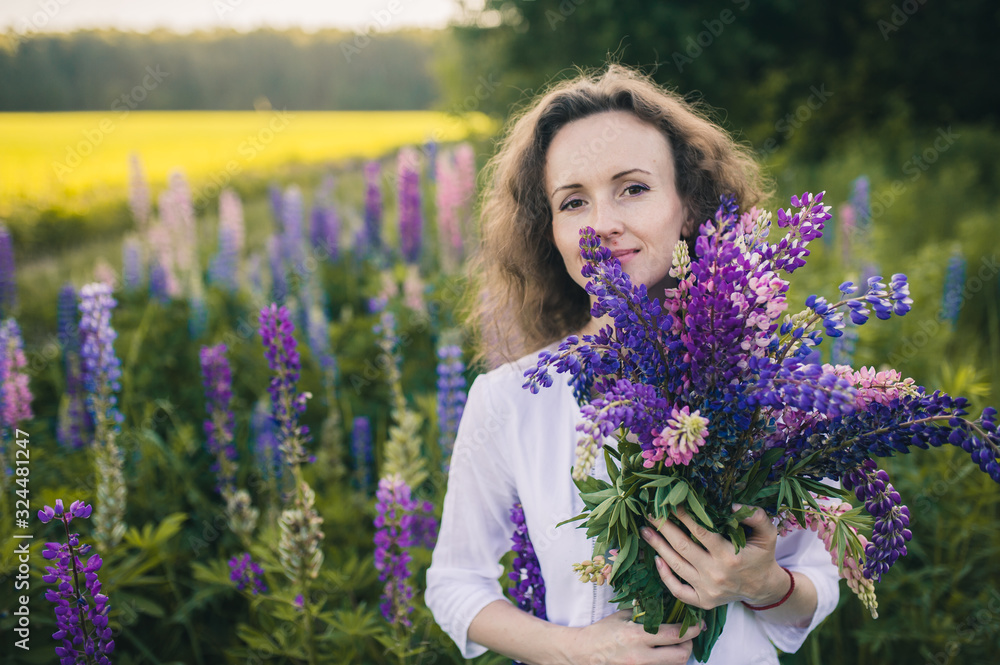 Beautiful woman in a white dress holds a large bouquet of lupins in the field. Beautiful woman in a white dress holds a large bouquet of lupins in the field.
