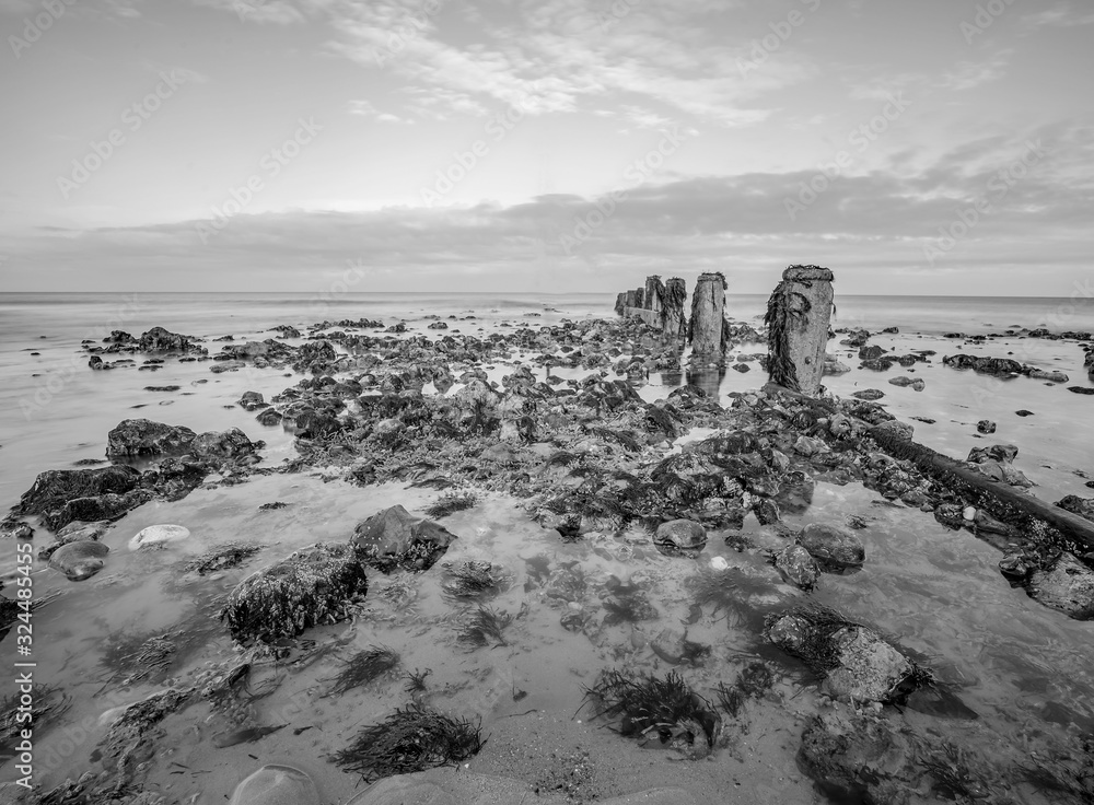 Seaweed covered rocks beside the wooden groyne on a sandy beach on the Norfolk coast captured on a bright but cold winters day