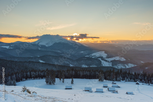 Charming snow-capped houses on a mountain Carpathian mountain valley  with magnificent views of peaks in winter.