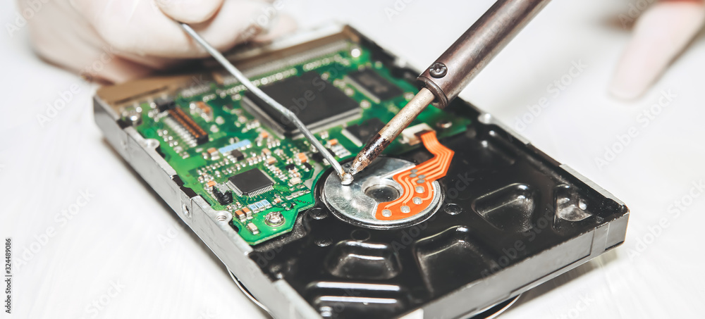 Man repairing hard disk. Inside details of the old personal computer. Broken PC. Soldering iron in hands. Man repairing hard disk. Inside details of the old personal computer. Broken PC. Soldering iron in hands.