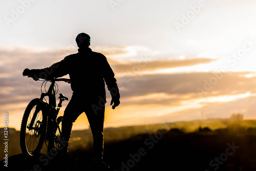 Mountain biker standing on top of a mountain with a bicycle  a beautiful sunset. Silhouette of a cyclist.