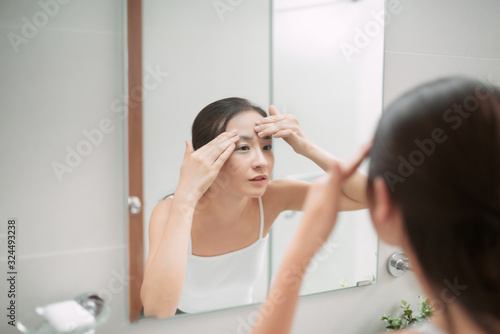 Beauty in mirror reflection. Over the shoulder view of beautiful woman touching her face while looking in the mirror