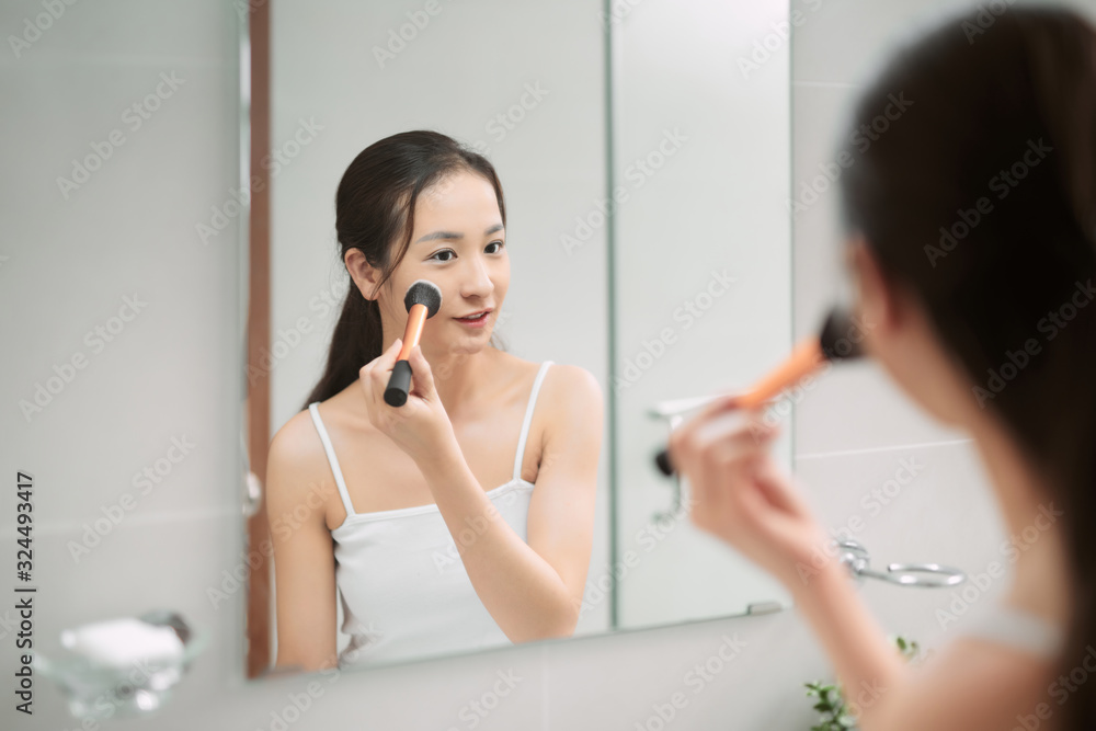 Portrait of attractive young adult woman applying blusher in her bathroom Portrait of attractive young adult woman applying blusher in her bathroom