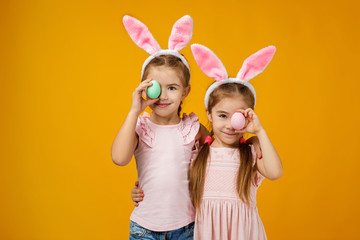 happy cute little child girls with pink bunny ears holding painted Easter eggs on studio yellow background. Easter day