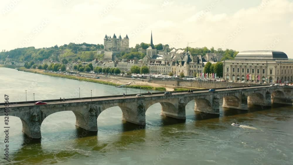 Aerial shot crossing a river with an old bridge and beautiful chateau in the background in France Aerial shot crossing a river with an old bridge and beautiful chateau in the background in France