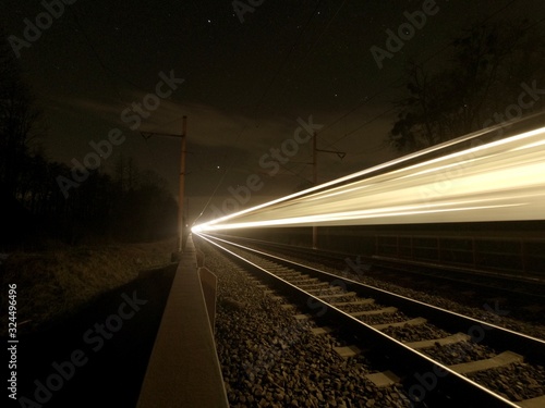 Focused night rails in the dark and blurry passing train. Night photo. Studenka. Czech Republic
