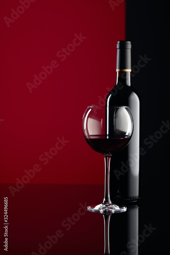 Glass and bottle of red wine on a black reflective background. Copy space.